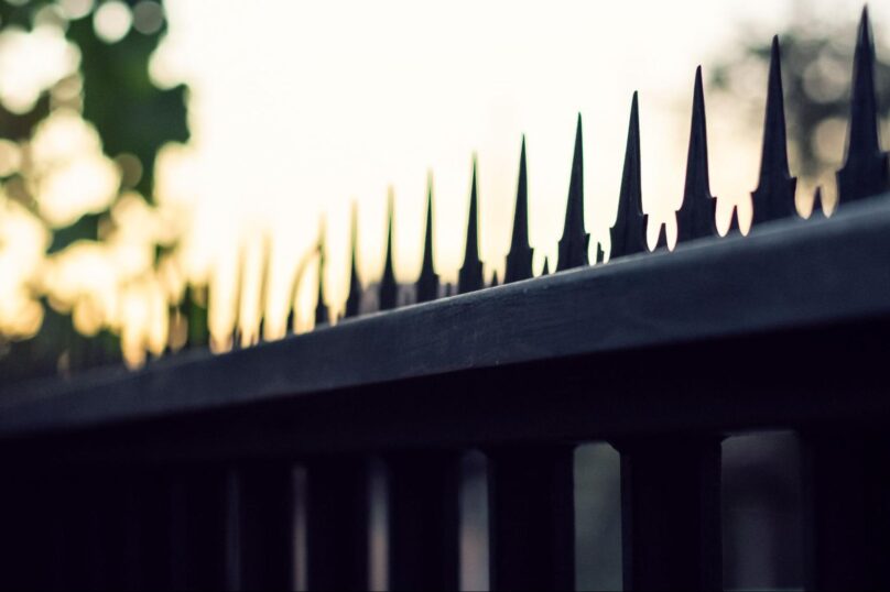 A silhouette of bird spikes on fences at sunrise.