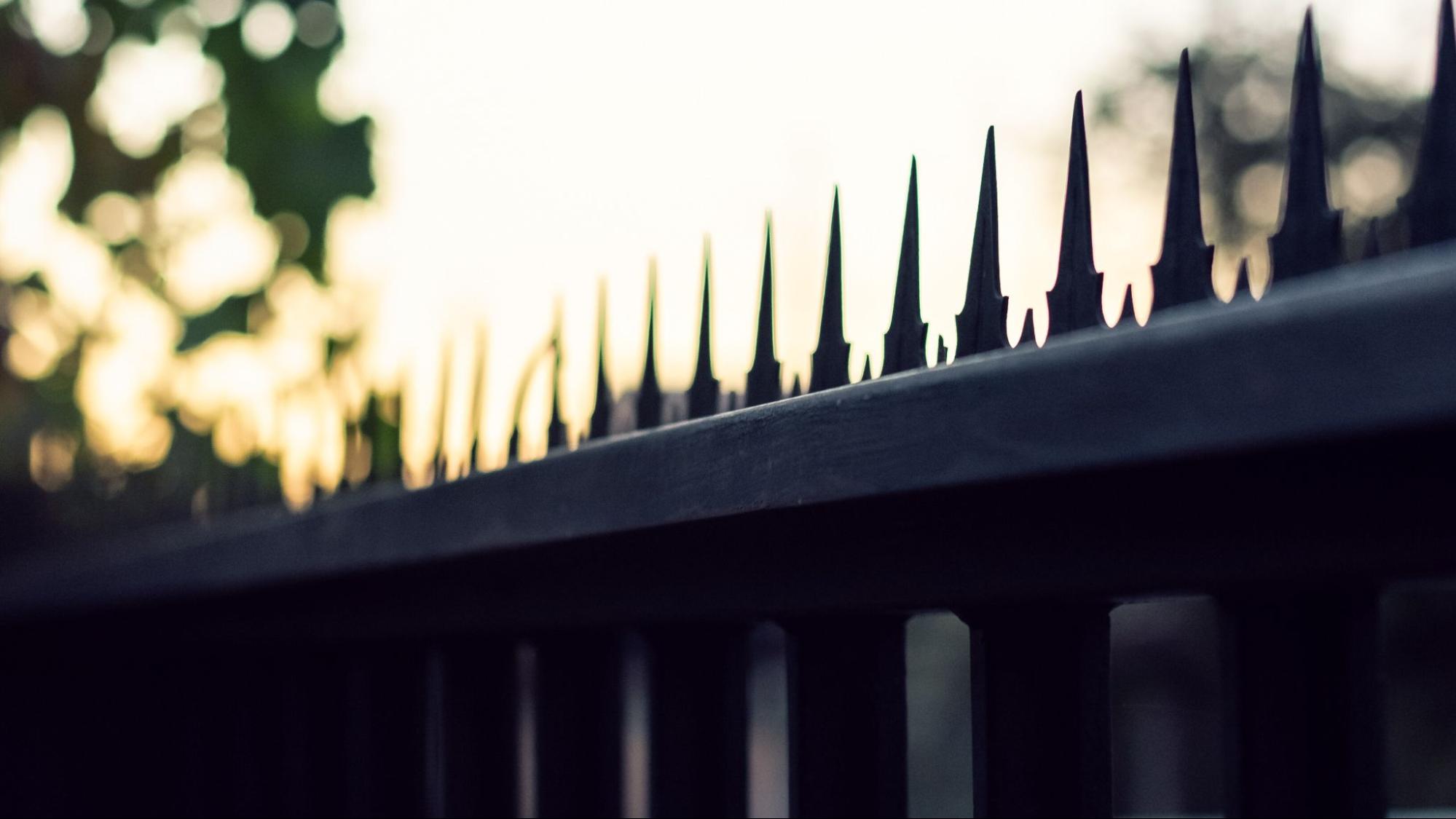 A silhouette of bird spikes on fences at sunrise.